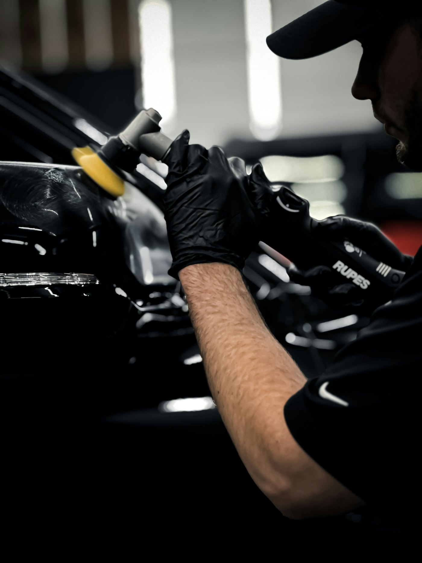 A detailer&rsquo;s gloved hands guiding a polisher across a panel