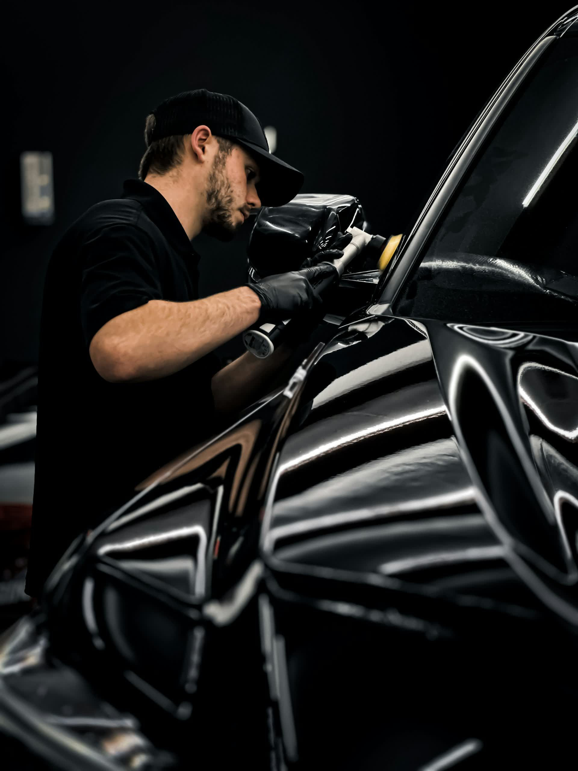 A detailer machine-polishing a black panel under shop lights