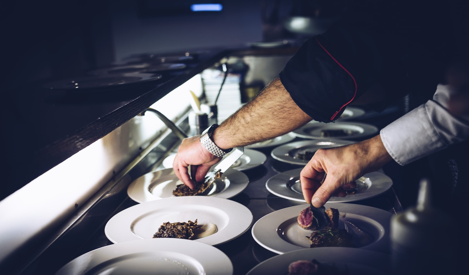 A chef plating dishes at the pass, both hands full mid-service